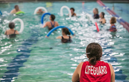 Lifeguard watching a group of people exercising with noodles in the pool