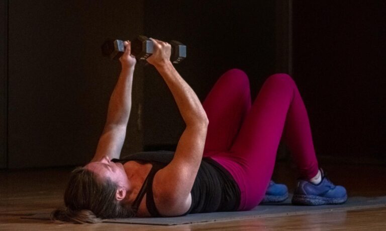 Woman laying on a mat using dumbbell hand weights