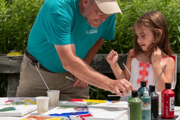 An adult and child painting on a canvas outside during the summer