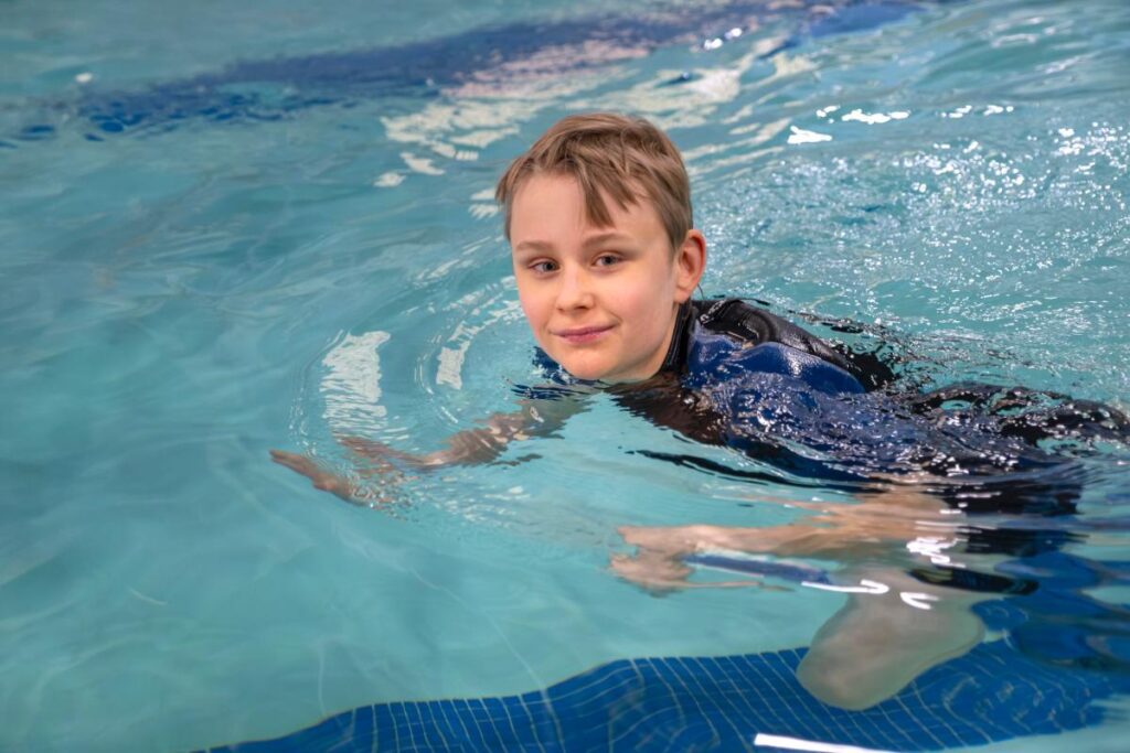 2025 Splash-A-Thon Ambassador James swimming in an indoor pool smiling at the camera