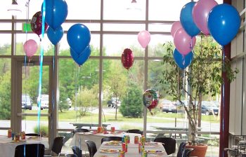 A room decorated for an event with balloons, banquet tables and place settings